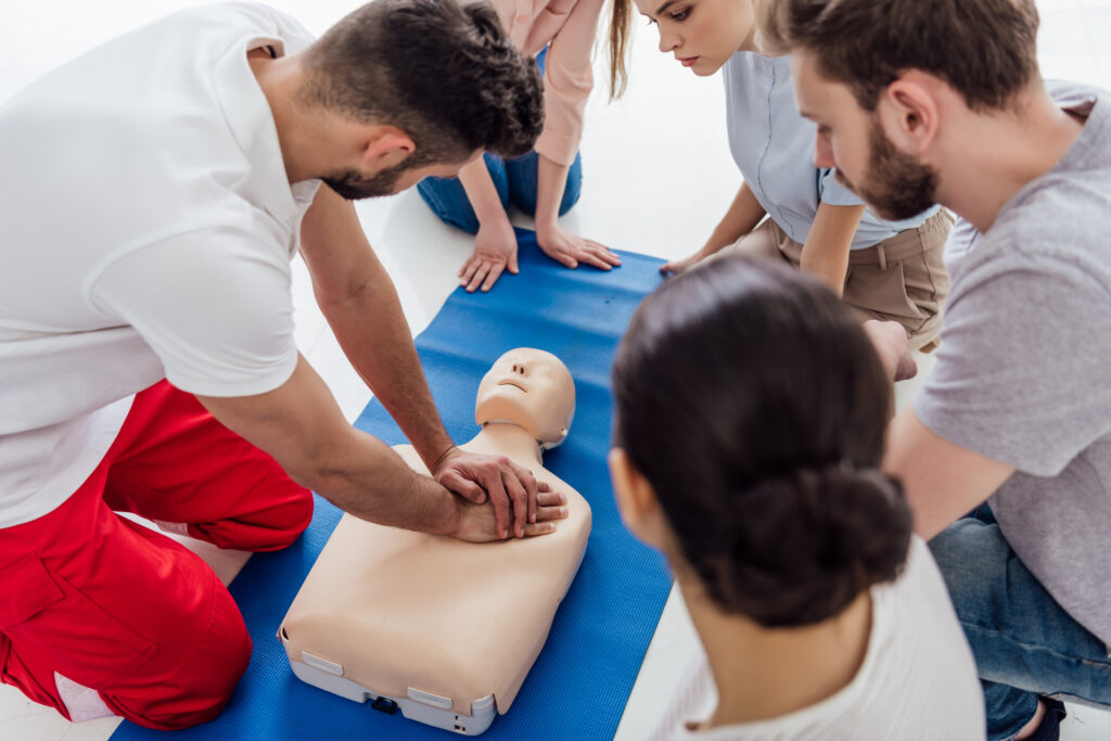 instructor performing cpr on dummy during first aid training with group of people