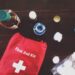 A red Emergency first aid kit on a wooden table with bandages, scissors, and medications.