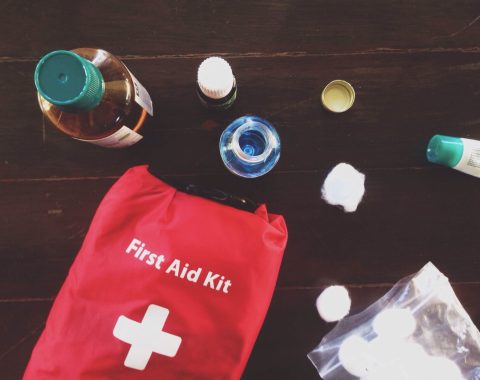 A red Emergency first aid kit on a wooden table with bandages, scissors, and medications.